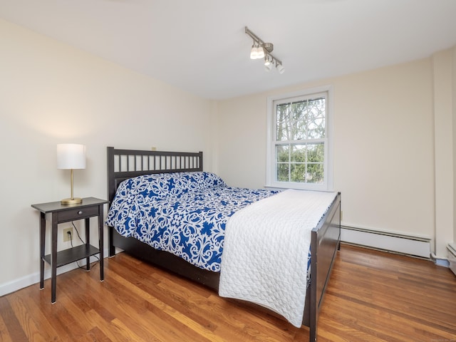 bedroom with track lighting, baseboards, baseboard heating, and wood finished floors