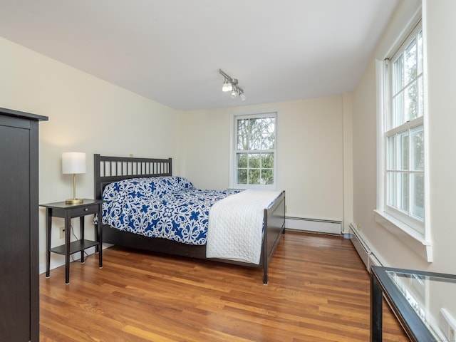 bedroom with a baseboard heating unit, multiple windows, and wood finished floors