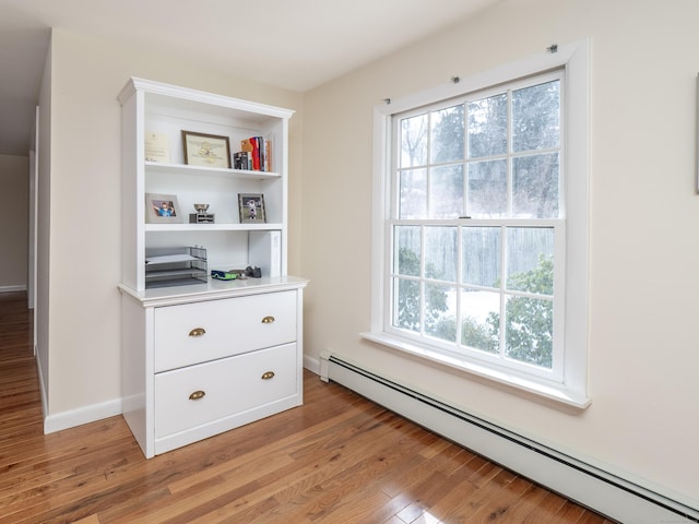 interior details with a baseboard heating unit, wood finished floors, and baseboards