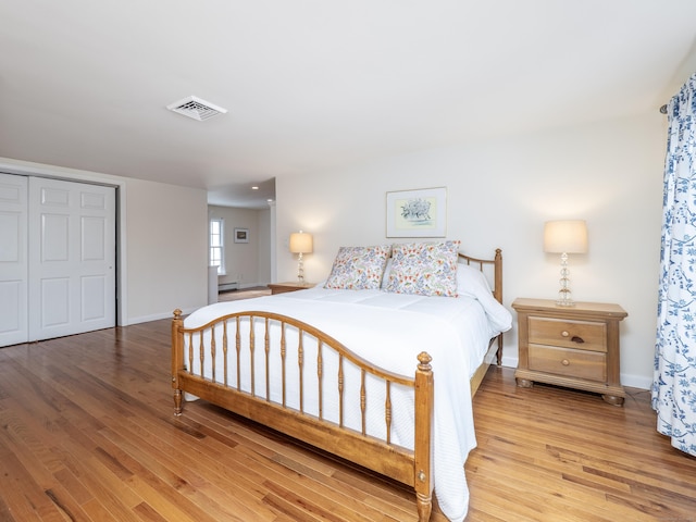 bedroom with a closet, visible vents, light wood-style flooring, and baseboards