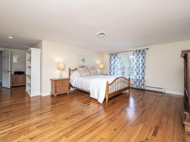 bedroom featuring baseboards, visible vents, baseboard heating, and hardwood / wood-style floors