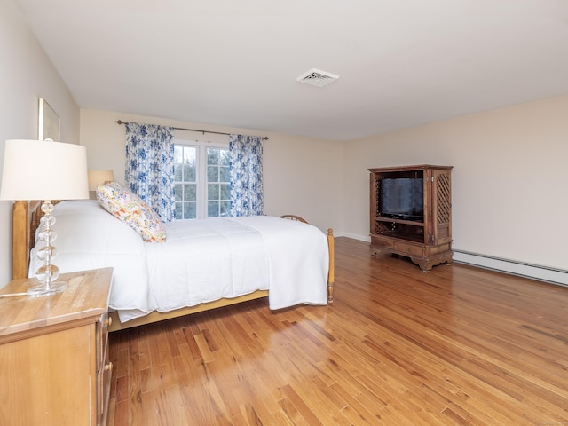 bedroom with a baseboard heating unit, light wood-type flooring, and visible vents