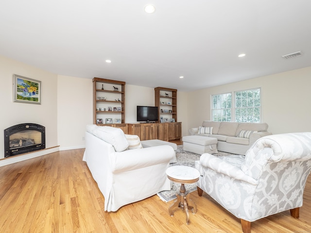 living area featuring recessed lighting, a fireplace with raised hearth, visible vents, and light wood finished floors