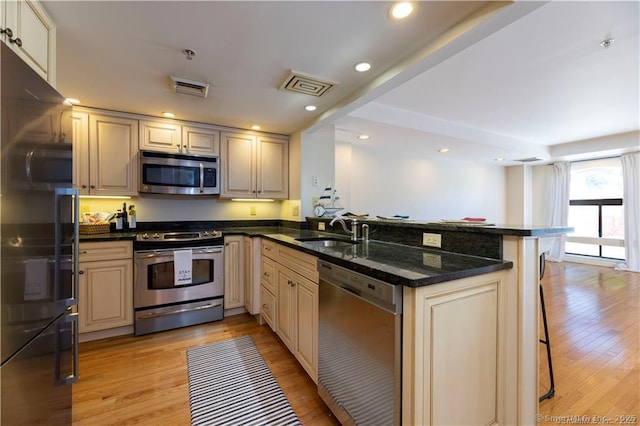 kitchen featuring visible vents, light wood-type flooring, a peninsula, stainless steel appliances, and a sink