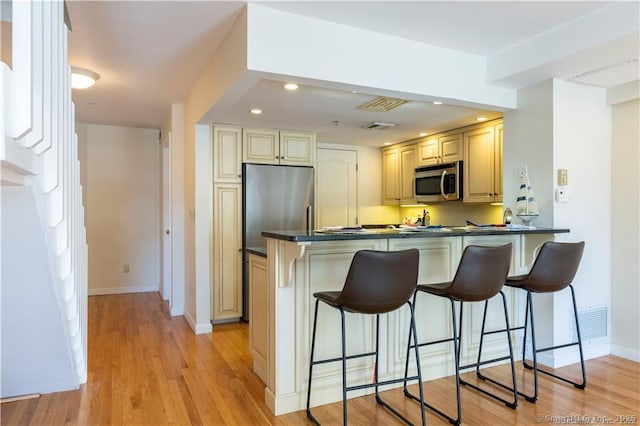 kitchen with dark countertops, a peninsula, stainless steel appliances, and a breakfast bar