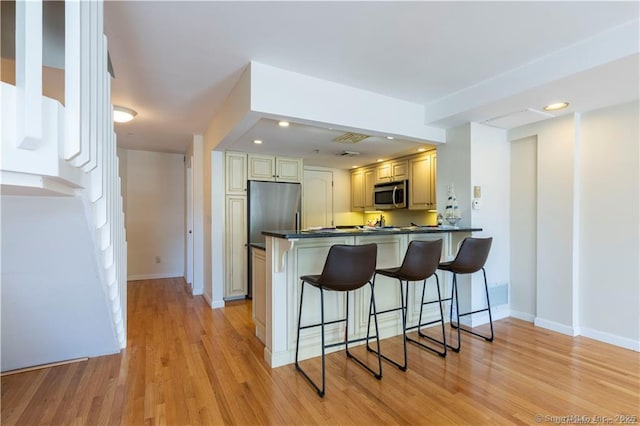 kitchen featuring light wood-style flooring, a kitchen breakfast bar, dark countertops, appliances with stainless steel finishes, and a peninsula