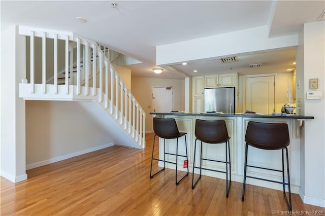 kitchen featuring baseboards, stainless steel refrigerator, light wood-style floors, dark countertops, and a kitchen breakfast bar