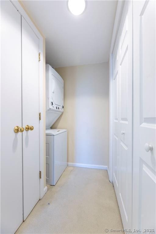 laundry room featuring laundry area, stacked washer / dryer, light colored carpet, and baseboards