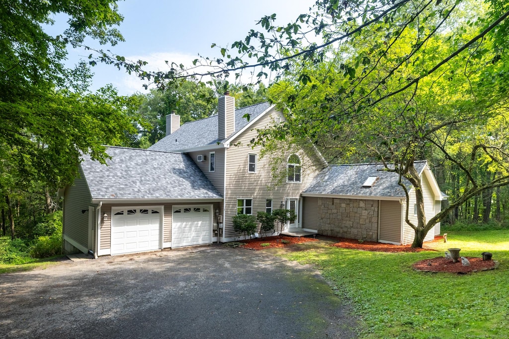 view of front of property featuring a garage, a shingled roof, driveway, a front lawn, and a chimney