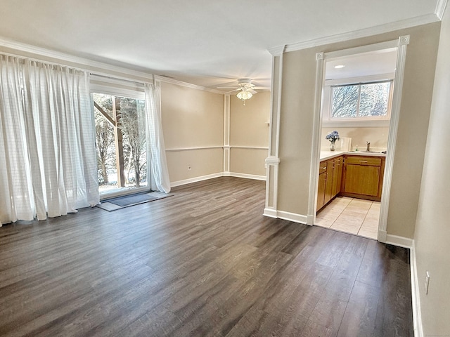 interior space featuring crown molding, light wood finished floors, baseboards, a ceiling fan, and ornate columns