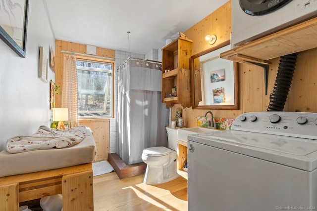 laundry room with laundry area, wood walls, wood finished floors, a sink, and washer / clothes dryer