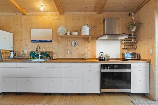 kitchen with beam ceiling, a sink, stainless steel oven, island range hood, and black electric cooktop