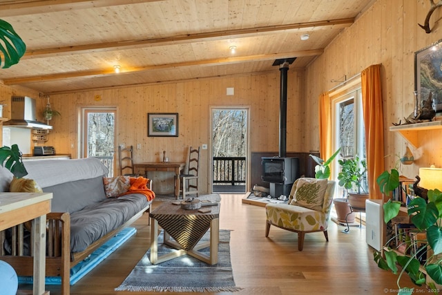 living area with a wealth of natural light, a wood stove, vaulted ceiling with beams, and wood finished floors