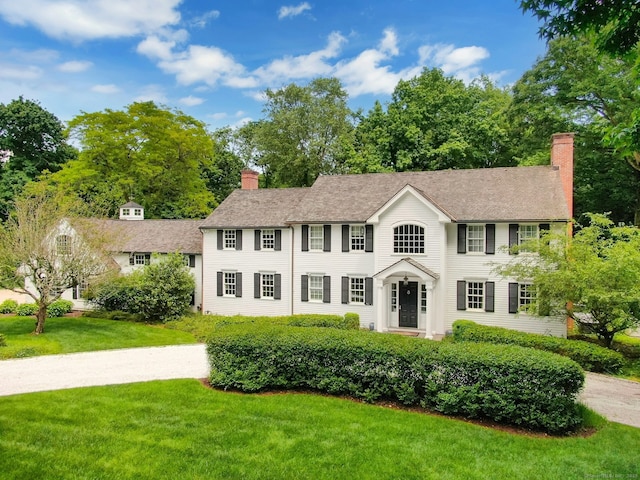 colonial home featuring driveway, a chimney, and a front yard