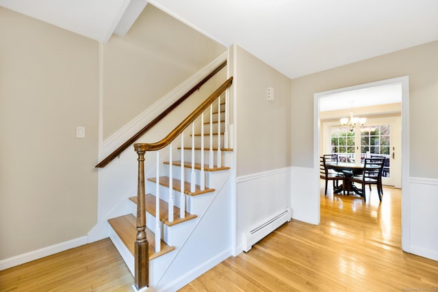 staircase with a notable chandelier, a baseboard radiator, wood finished floors, and wainscoting