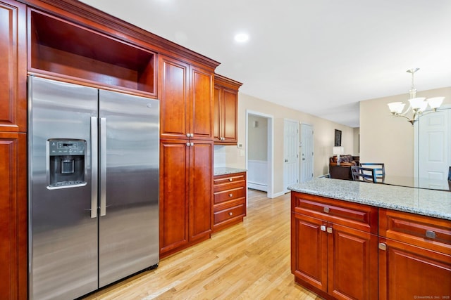 kitchen featuring light wood-type flooring, light stone countertops, reddish brown cabinets, stainless steel fridge, and pendant lighting