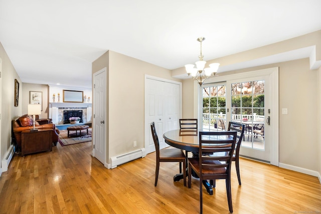 dining space featuring a baseboard radiator, a fireplace, light wood-style flooring, and an inviting chandelier