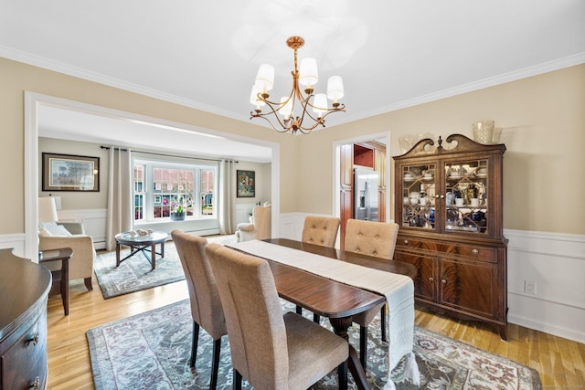 dining room with ornamental molding, light wood-type flooring, a chandelier, and wainscoting