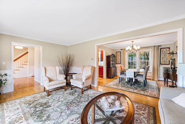 living room featuring a wainscoted wall, a notable chandelier, crown molding, light wood finished floors, and stairs