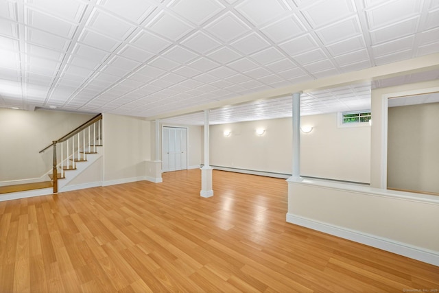 below grade area featuring light wood-type flooring, baseboards, baseboard heating, and stairs