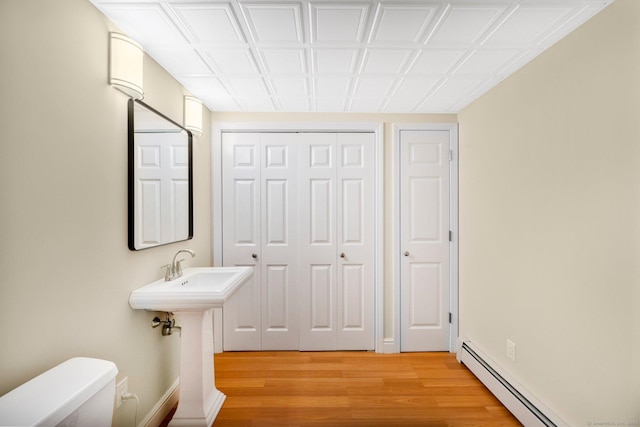 half bath with a baseboard heating unit, a closet, wood finished floors, and toilet