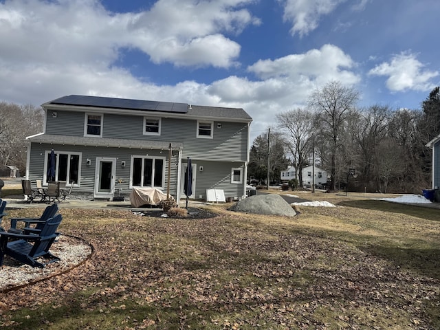 back of property with a patio area, solar panels, and a lawn