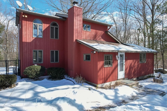 view of snowy exterior with fence and a chimney