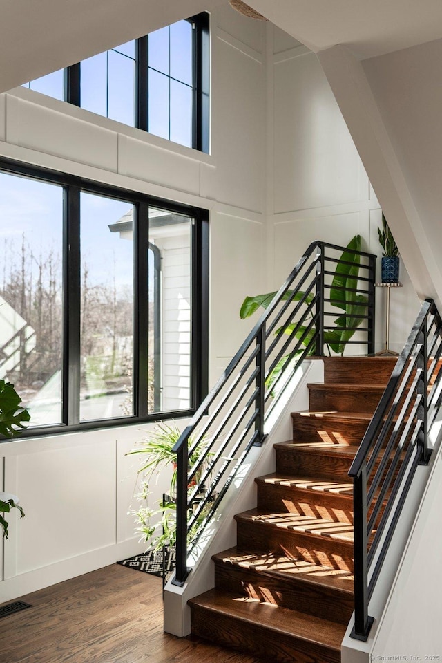 stairs featuring wood finished floors, a high ceiling, a healthy amount of sunlight, and visible vents