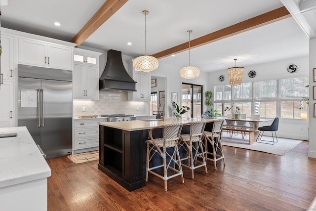 kitchen featuring tasteful backsplash, beamed ceiling, built in fridge, custom exhaust hood, and a sink