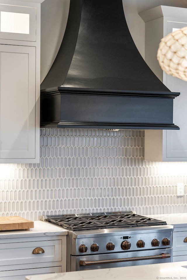 kitchen featuring premium range hood, stainless steel range with gas cooktop, white cabinets, and light countertops