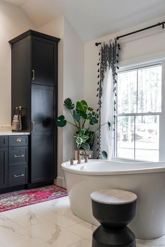 full bathroom with vaulted ceiling, a freestanding tub, and marble finish floor