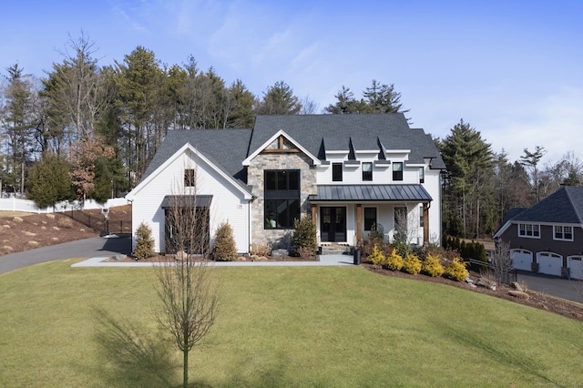 modern farmhouse featuring a garage, a front lawn, a standing seam roof, stone siding, and metal roof