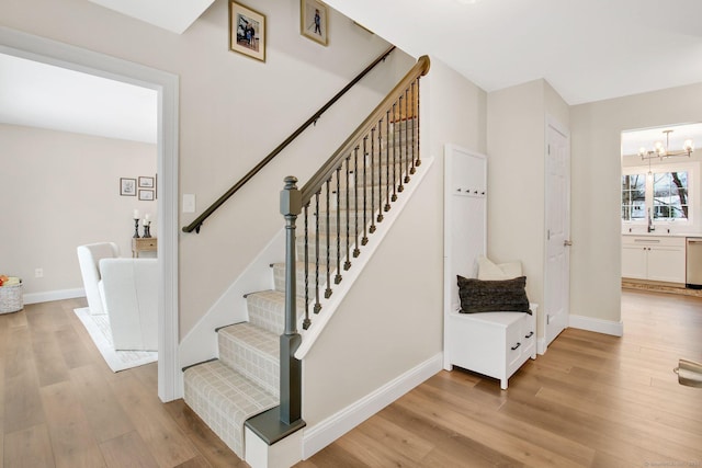 stairs featuring an inviting chandelier, baseboards, and wood finished floors