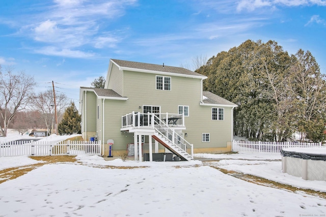 snow covered property featuring a deck, stairway, and fence