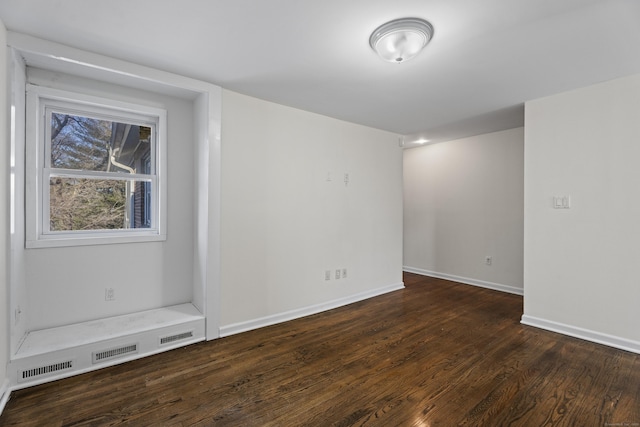 spare room with baseboards and dark wood-style flooring