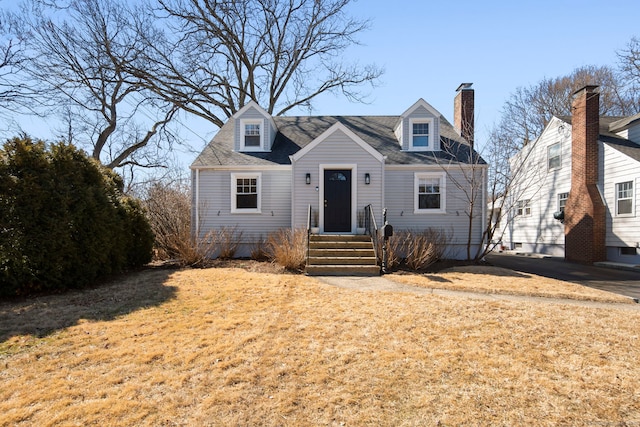 cape cod house featuring a shingled roof, a chimney, and a front lawn