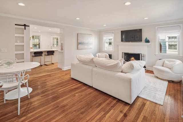 living room featuring light wood-style floors, a barn door, crown molding, and a wealth of natural light