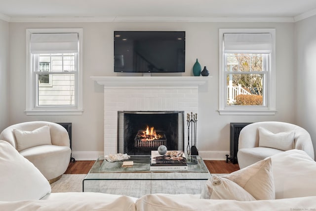 living room with a brick fireplace, crown molding, baseboards, and wood finished floors