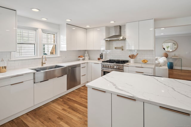 kitchen featuring stainless steel appliances, white cabinetry, a sink, wall chimney range hood, and modern cabinets