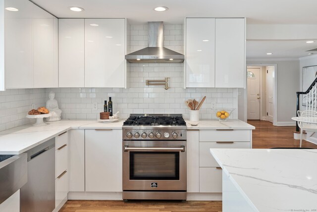 kitchen with light stone counters, white cabinetry, wall chimney range hood, appliances with stainless steel finishes, and modern cabinets