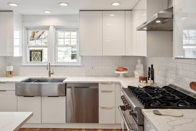 kitchen with stainless steel appliances, a sink, white cabinets, wall chimney range hood, and modern cabinets