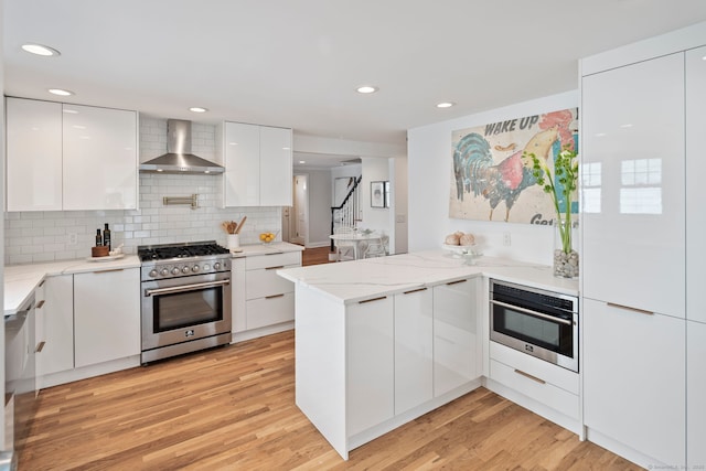 kitchen featuring stainless steel appliances, a peninsula, wall chimney exhaust hood, and modern cabinets