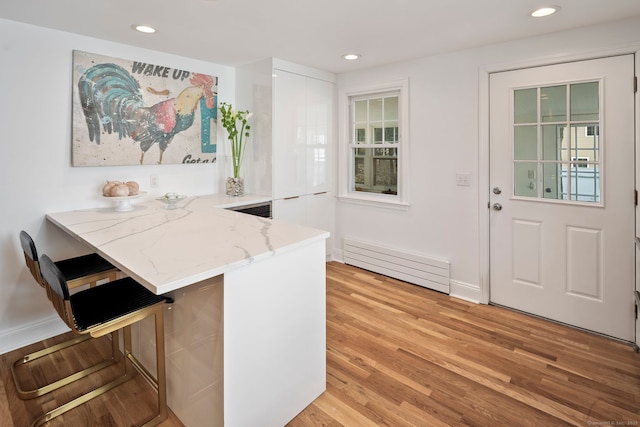 kitchen with light wood finished floors, recessed lighting, baseboard heating, light stone countertops, and a peninsula