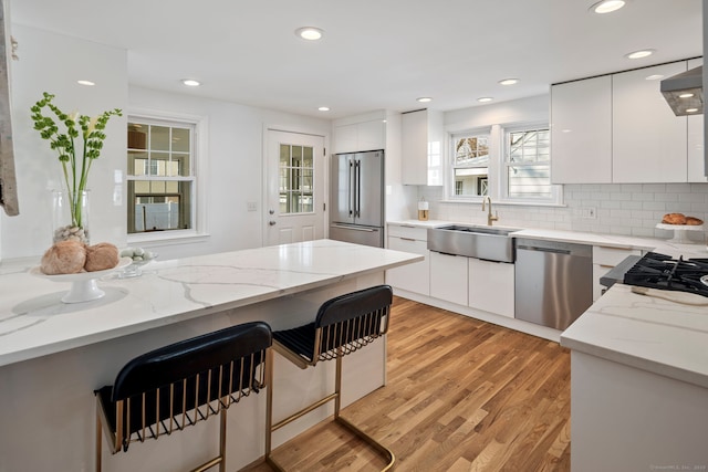 kitchen with stainless steel appliances, light wood-style floors, white cabinets, a sink, and modern cabinets