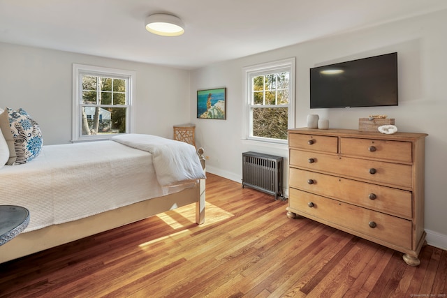 bedroom with multiple windows, light wood finished floors, and radiator heating unit