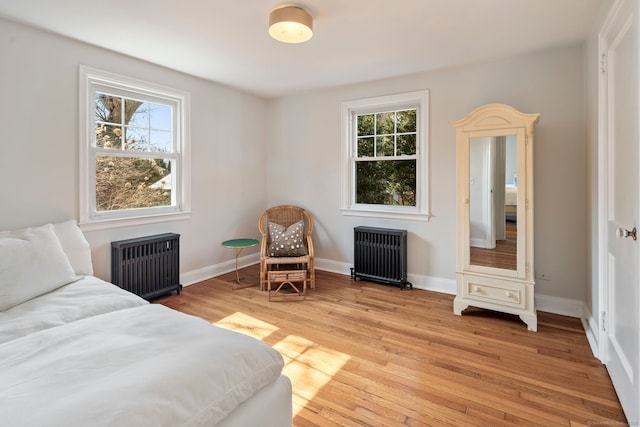 bedroom featuring light wood-type flooring, radiator, multiple windows, and radiator heating unit