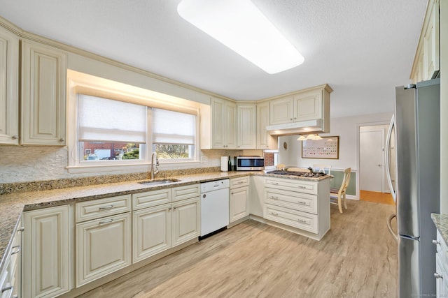 kitchen with under cabinet range hood, cream cabinets, appliances with stainless steel finishes, and a sink