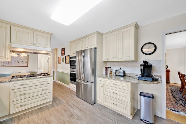 kitchen with under cabinet range hood, cream cabinetry, stainless steel appliances, and light wood-type flooring