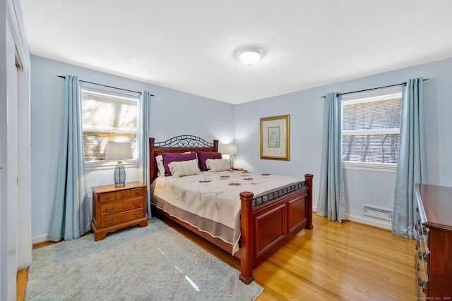 bedroom featuring multiple windows, baseboards, light wood-type flooring, and baseboard heating