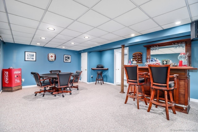 carpeted dining space with a paneled ceiling and indoor bar